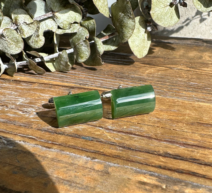Green jade cufflinks with sterling silver settings resting on a rustic wooden surface.
