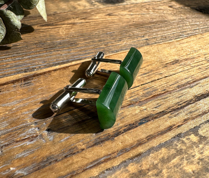 Pair of green jade cufflinks with rectangular stones in polished silver settings on a wooden surface.