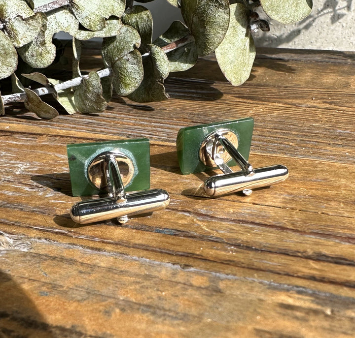 Back view of green jade cufflinks with silver toggle bars on a wood surface.