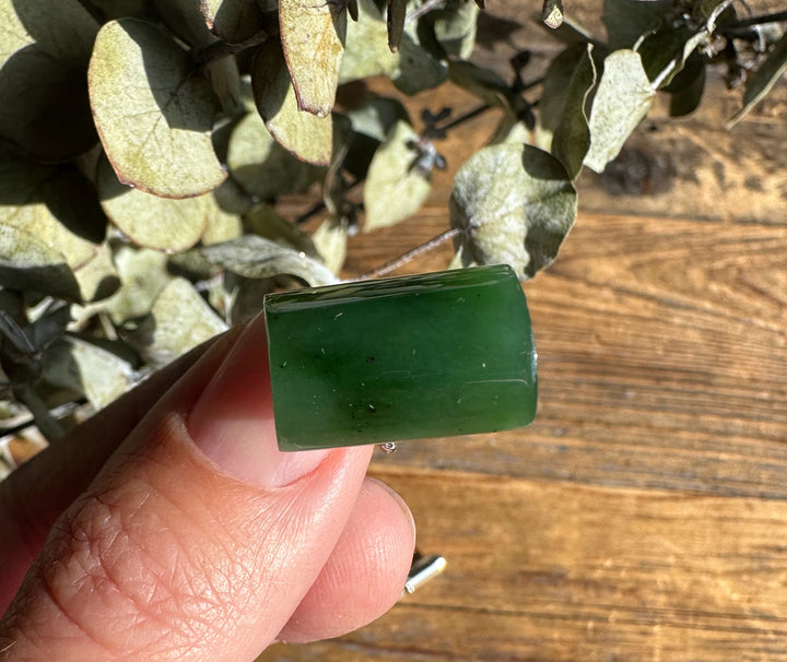 Close up of green jade rectangular piece held between fingers over a wooden surface.