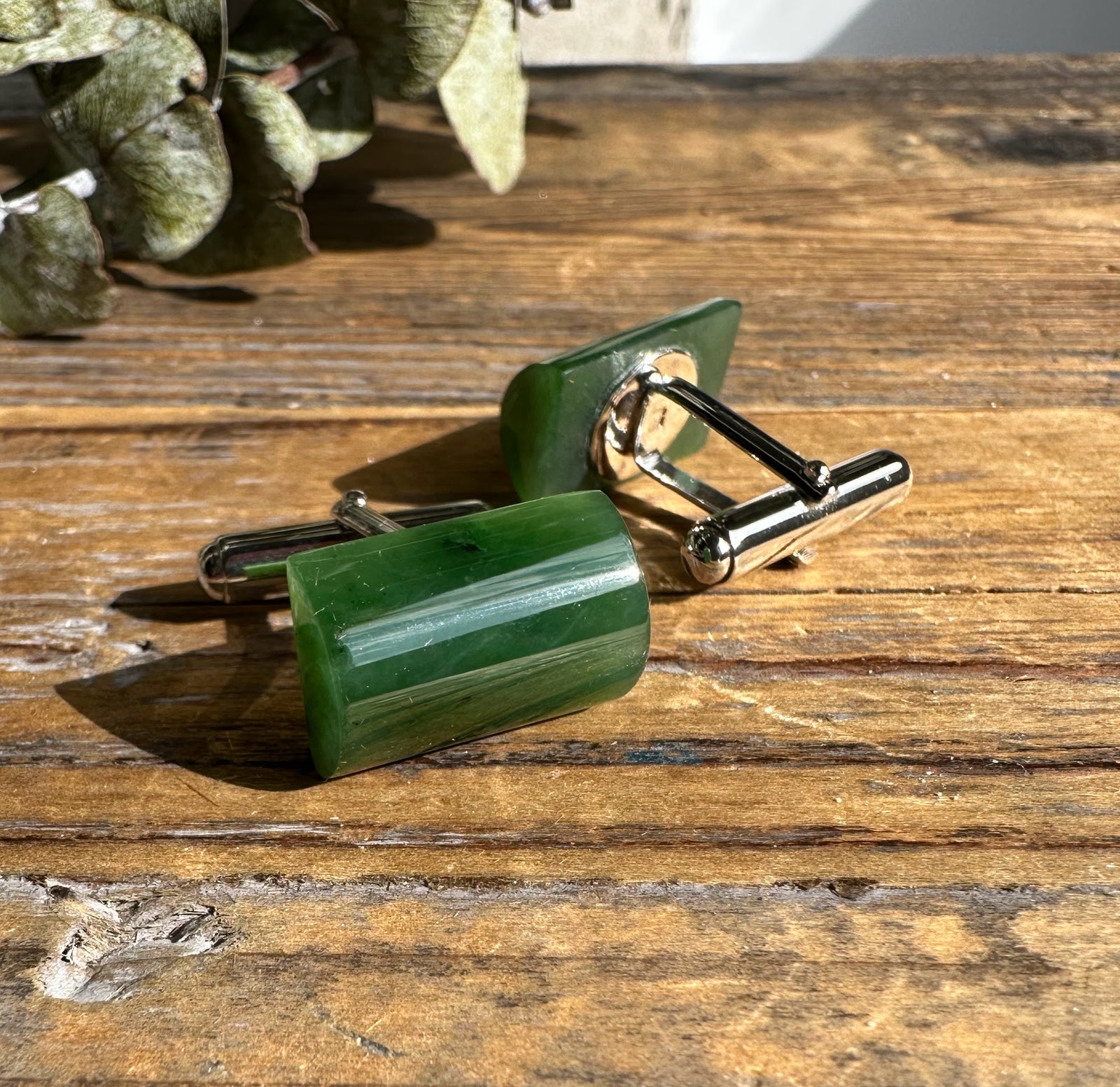 Green jade cufflinks with sterling silver mounts on a rustic wooden surface.