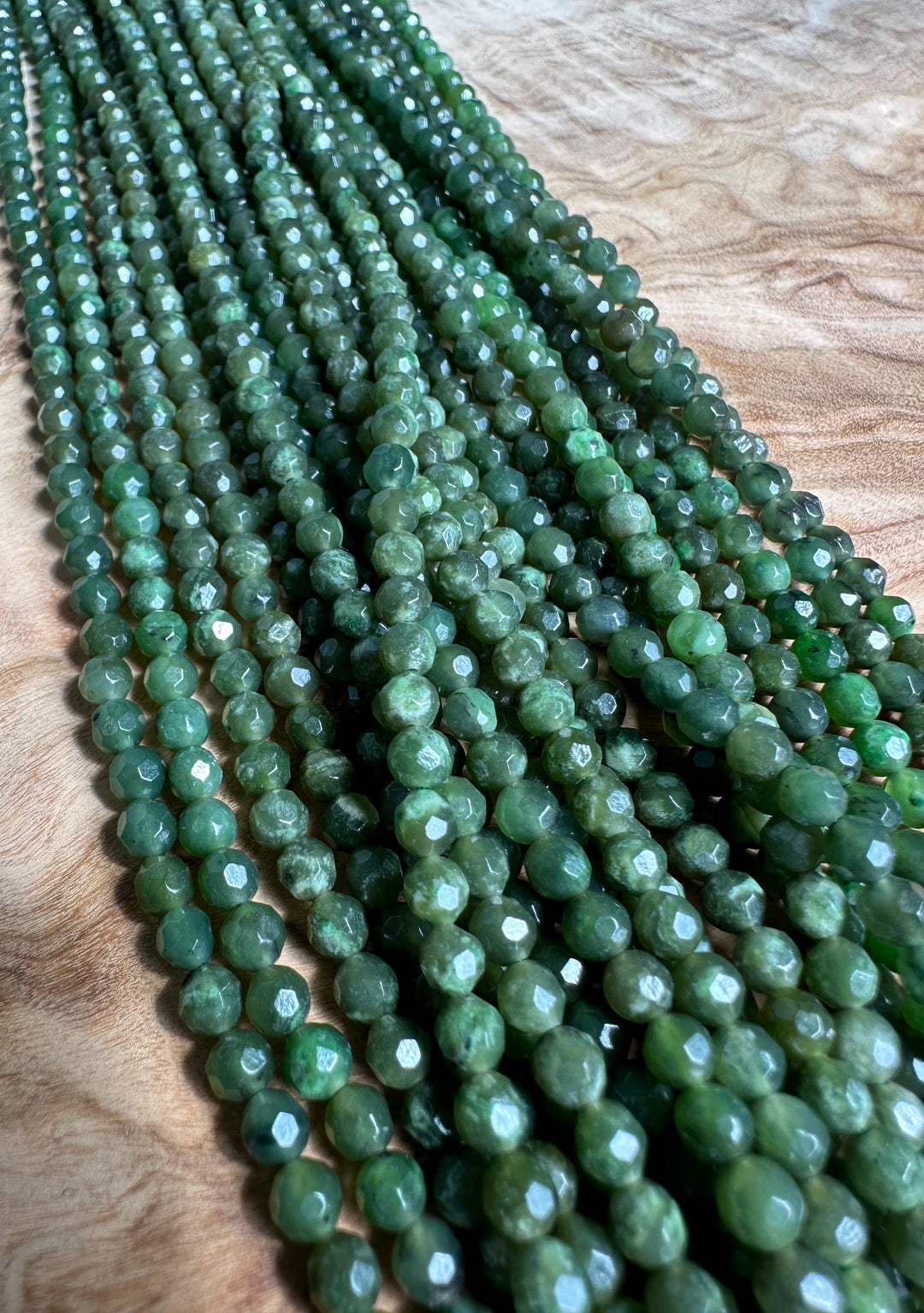 Close up of green faceted 4mm beads in unstrung strands on a wooden surface