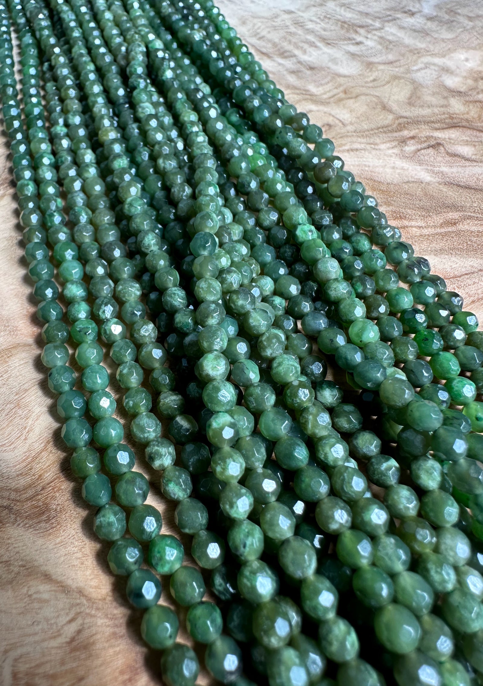 Close up of green faceted 4mm beads in unstrung strands on a wooden surface