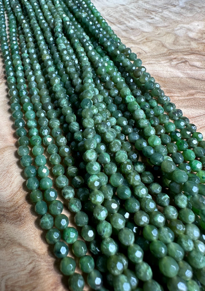 Close up of green faceted 4mm beads in unstrung strands on a wooden surface