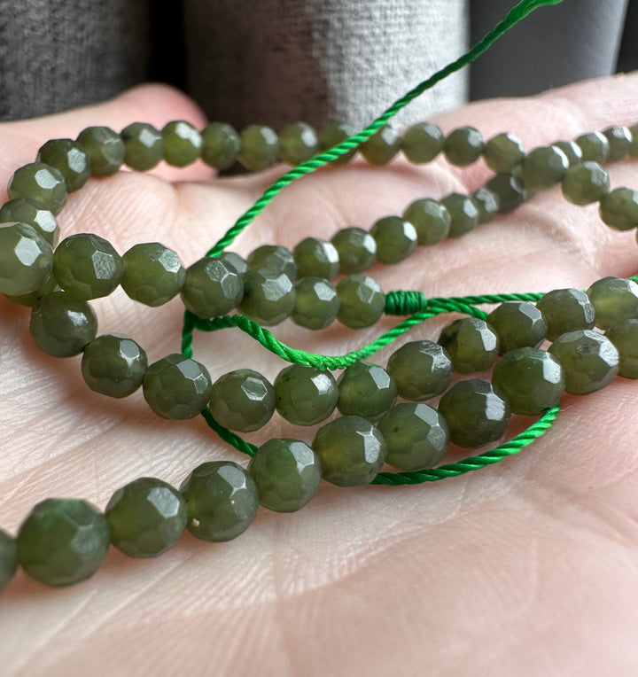Olive green faceted 4mm beads unstrung shown on a hand with a bright green cord nearby