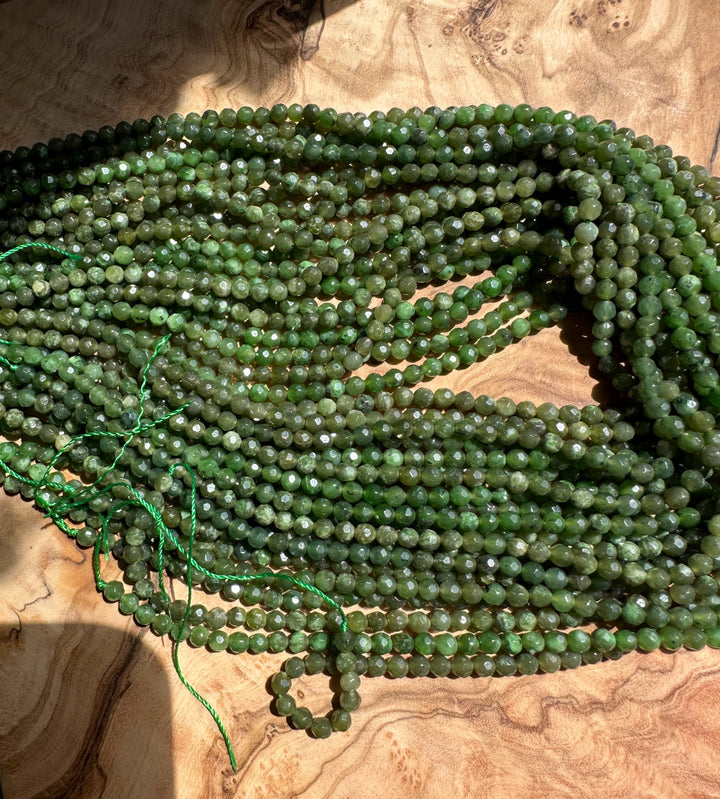 Dense pile of green low grade faceted 4mm beads spilled on a wood surface with a green cord entwined