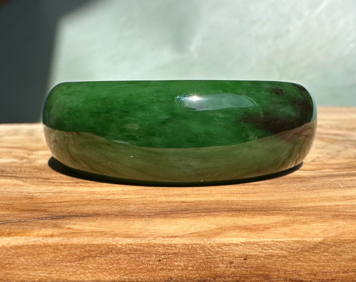 AA Bangle 50 x 18mm in green jade resting on a wooden surface.
