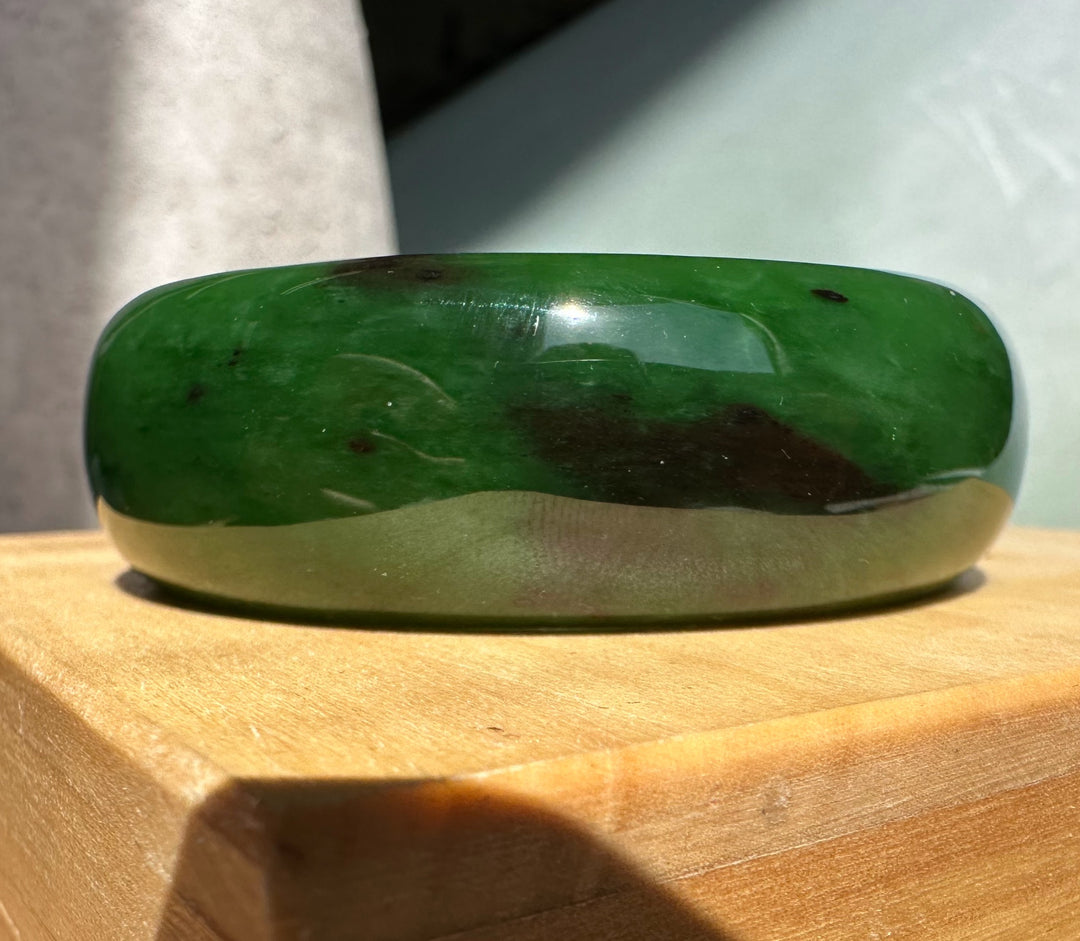 AA Bangle 50 x 18mm in green jade on a wooden surface with light reflections.