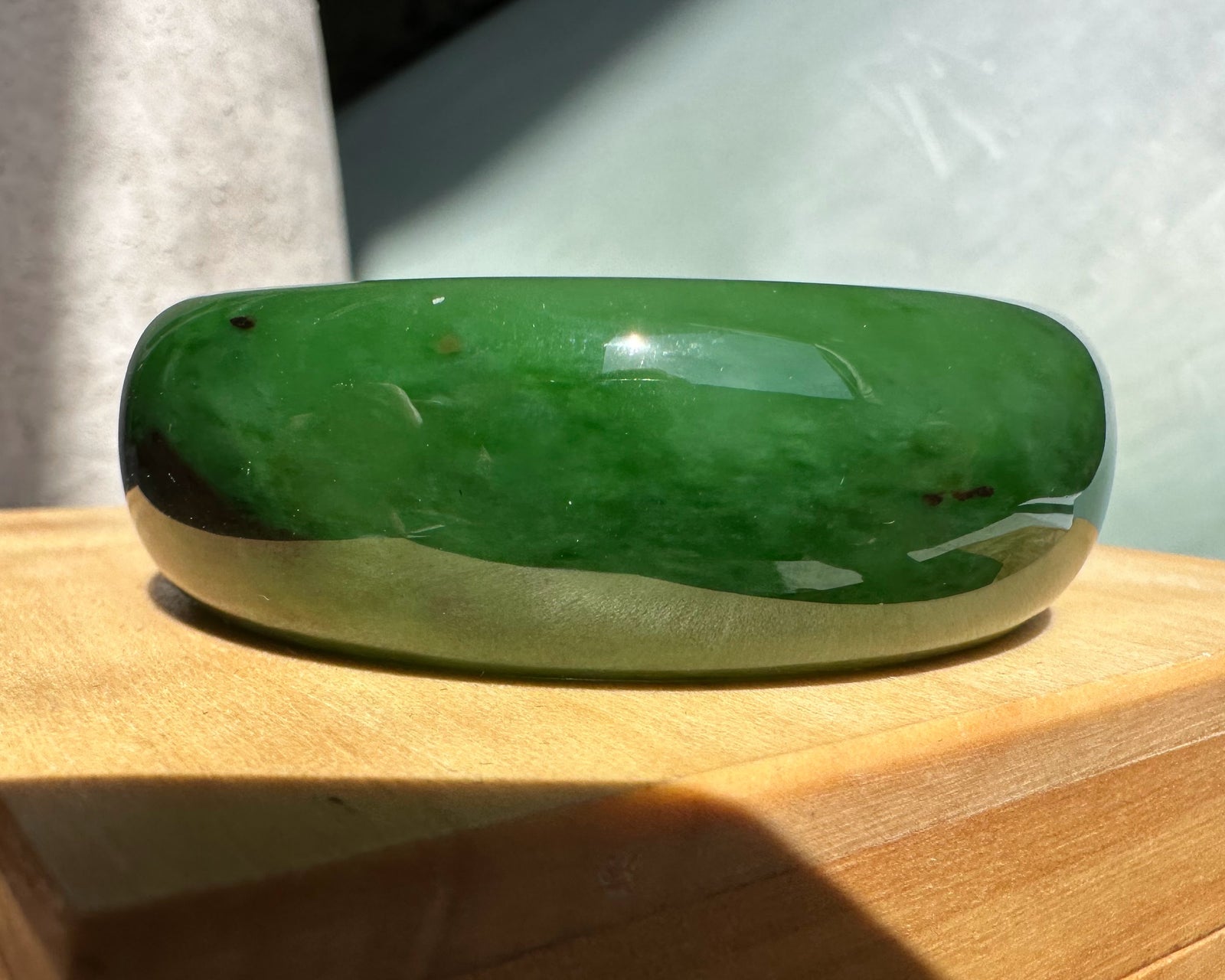 Green jade AA Bangle resting on a wooden surface with a glossy finish