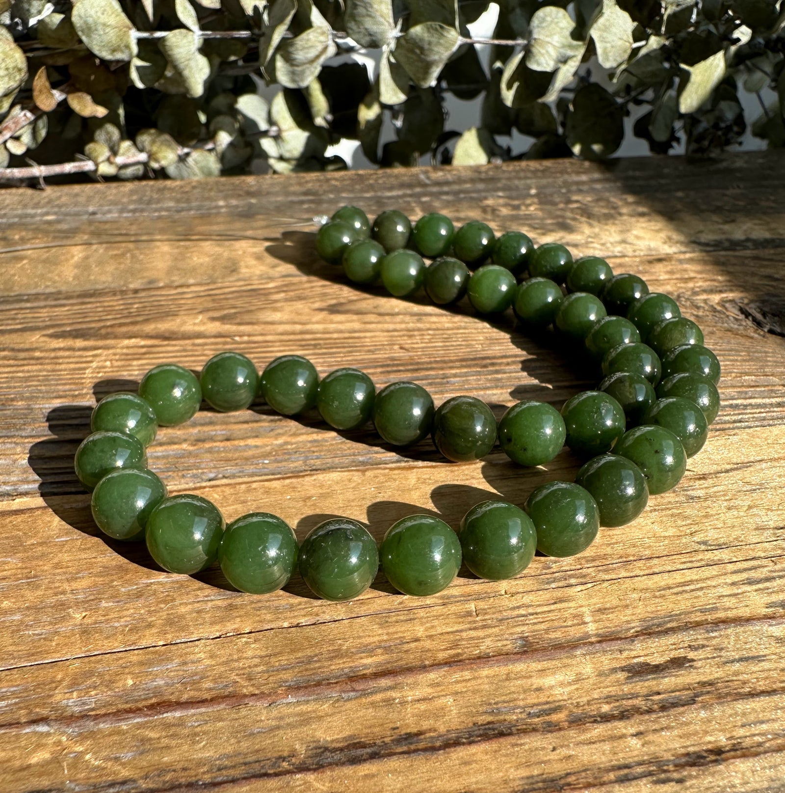 Unstrung Canadian 10mm carving grade jade beads laid in a loose loop on a wooden surface.