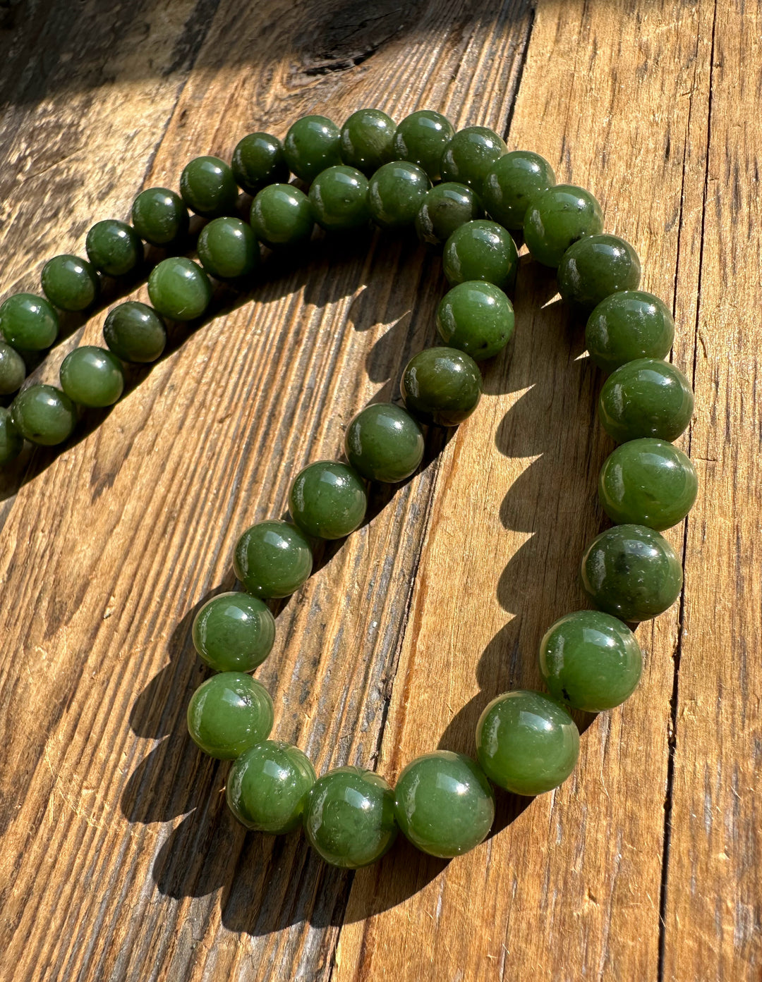 Close up of unstrung Canadian 10mm carving grade jade beads on a wooden surface.