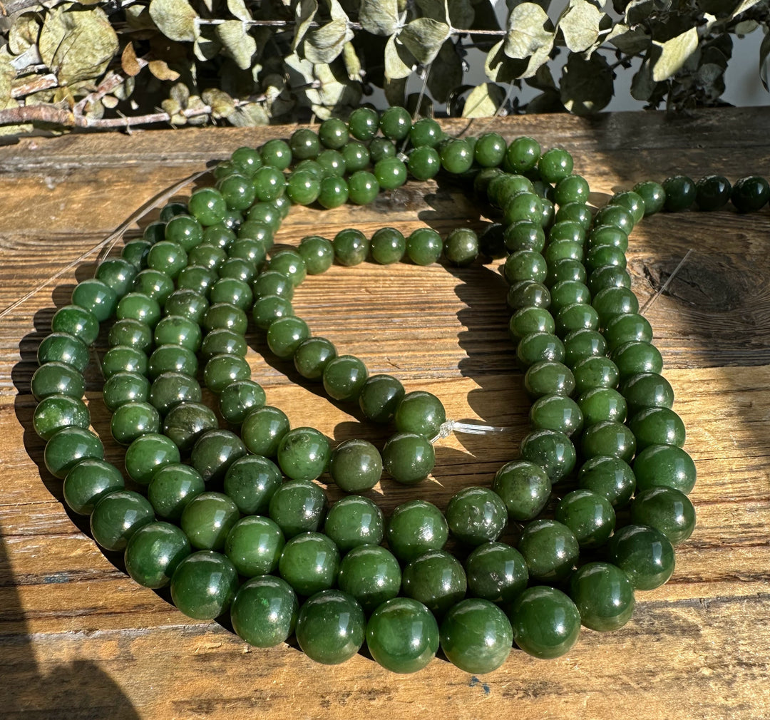 Multiple strands of unstrung Canadian 10mm carving grade green beads spread across a wooden table