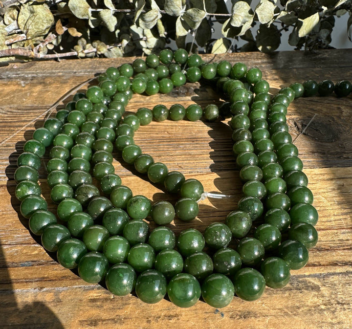 Multiple strands of unstrung Canadian 10mm carving grade green beads spread across a wooden table