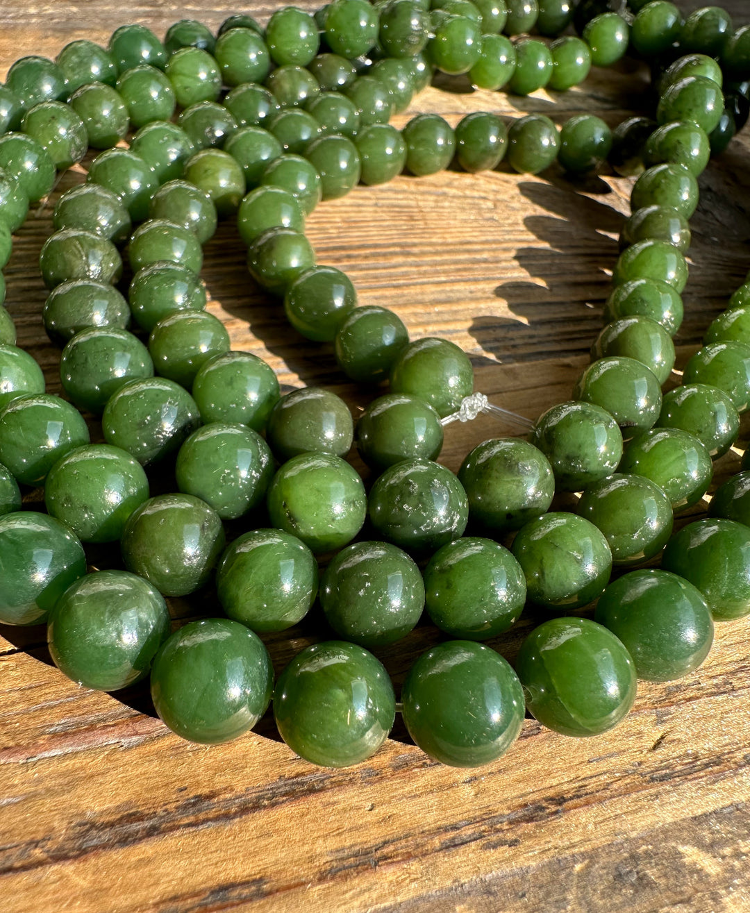 Close-up of glossy green 10mm carving grade beads on a wooden surface