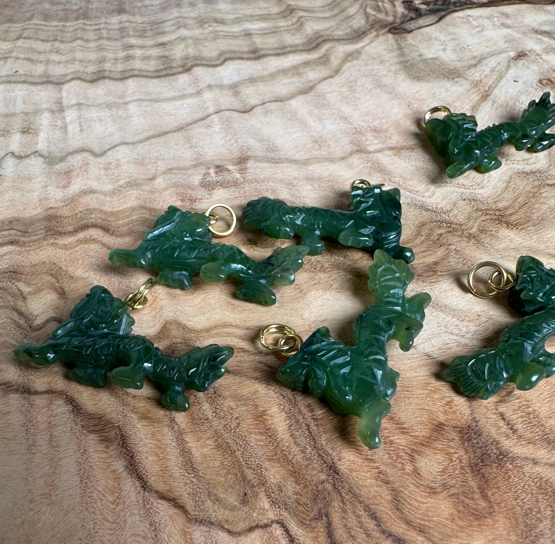Dark green carved jade dragon charms with gold loops on a wood surface