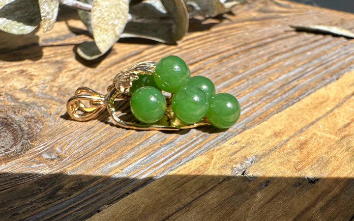Vintage jade grape pendant with five round green beads set in a gold holder on a wooden surface