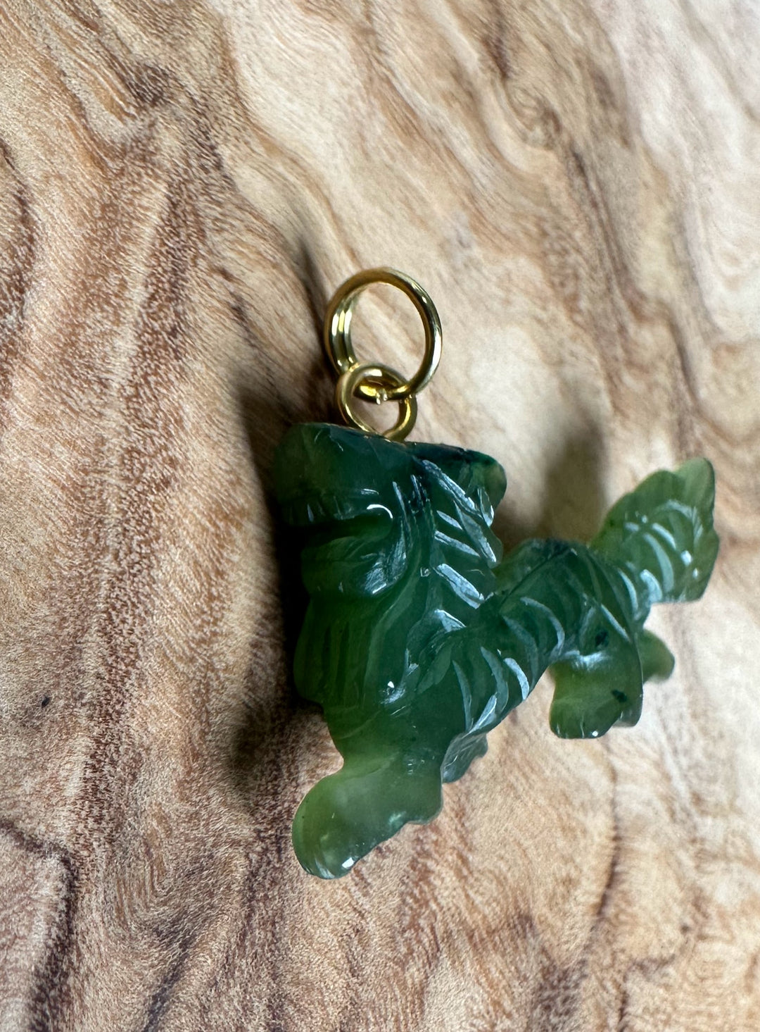 Single green jade dragon pendant on a brown cord with a gold ring at the top