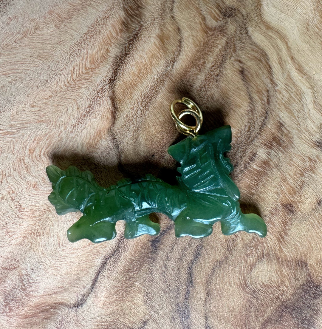Canadian Jade Dragon pendant in green with gold bail on wood surface