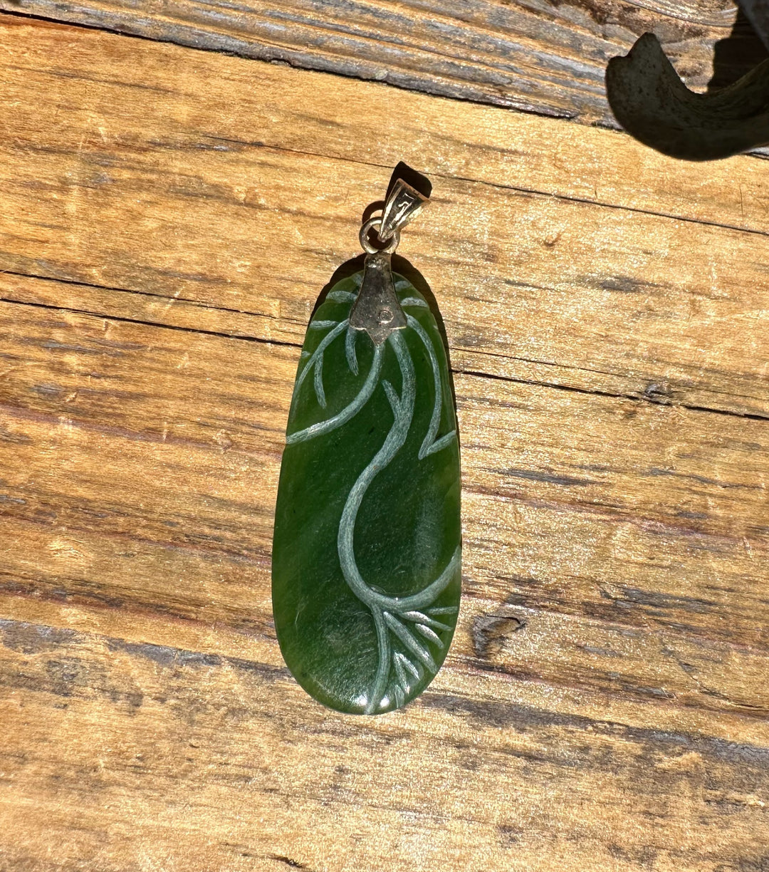 Green jade pendant with a carved leaf pattern along an elongated oval, hanging from a silver chain