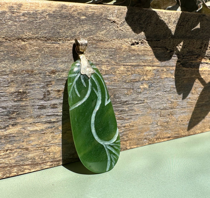 Oval green jade pendant with pale carved vine design and a gold bail