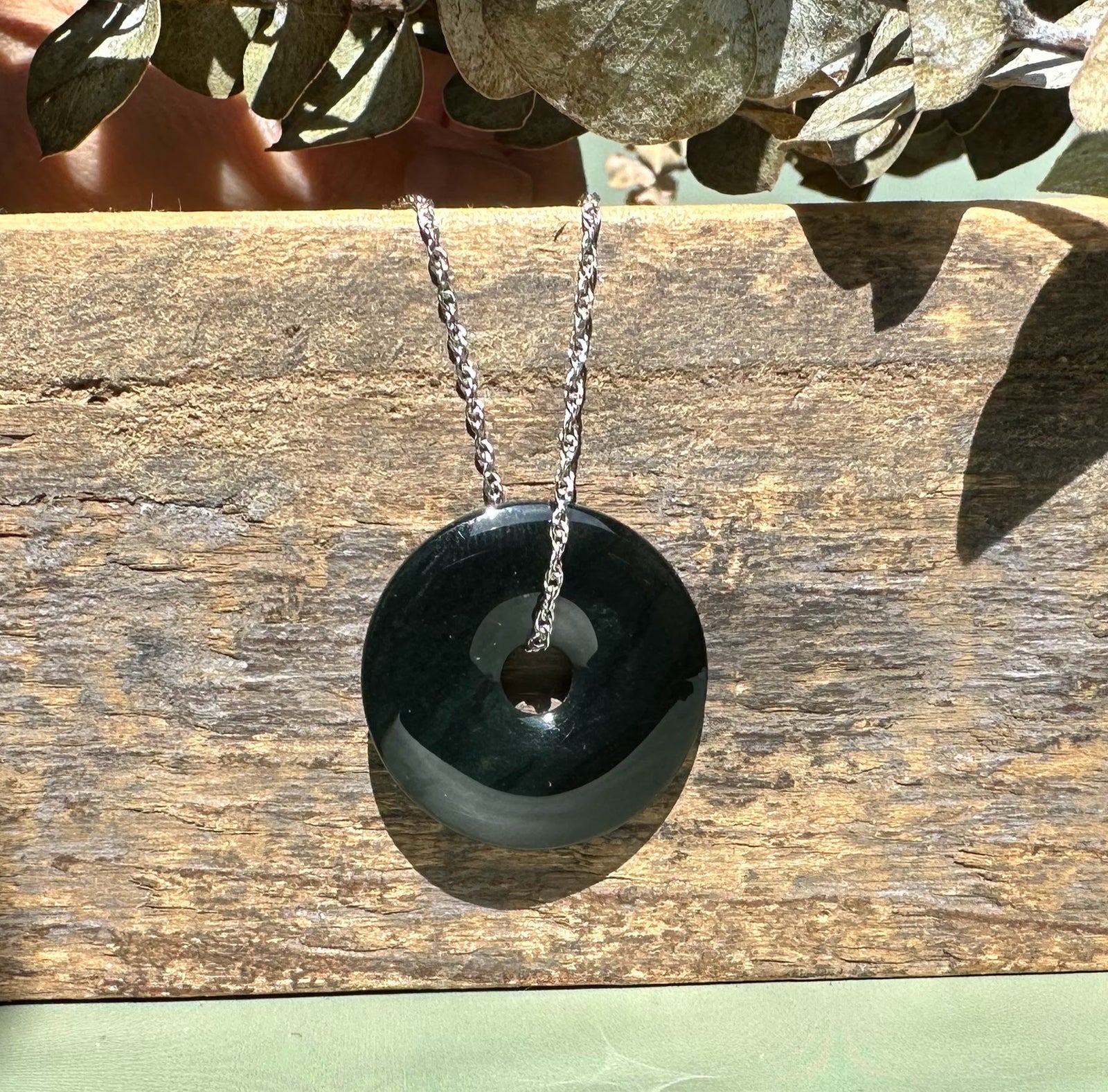 Australian jade donut pendant with a central hole and glossy dark green surface on weathered wood