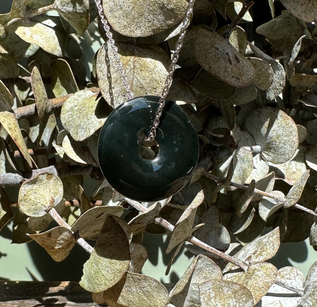 Dark green Australian Jade donut pendant on a silver chain nestled among dried eucalyptus leaves.