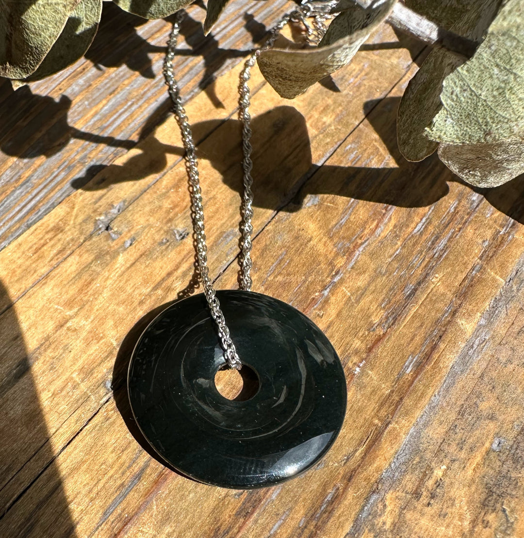 Dark green jade donut pendant on a silver chain resting on a wooden surface.