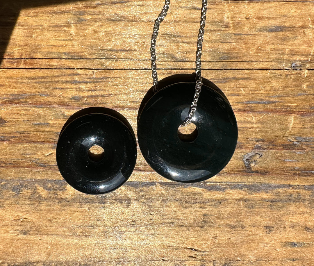 Two dark green jade donut pendants in small and large sizes on silver chains laid on wood.