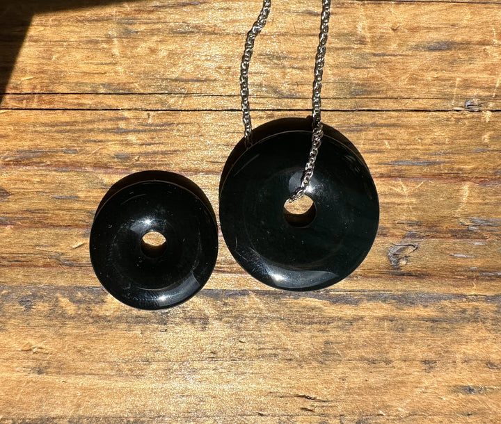 Two dark green jade donut pendants in small and large sizes on silver chains laid on wood.