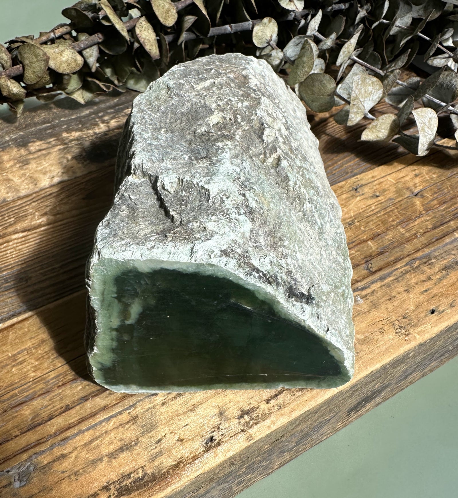 Siberian nephrite rough with a dark green interior and gray rocky exterior on a wooden surface.