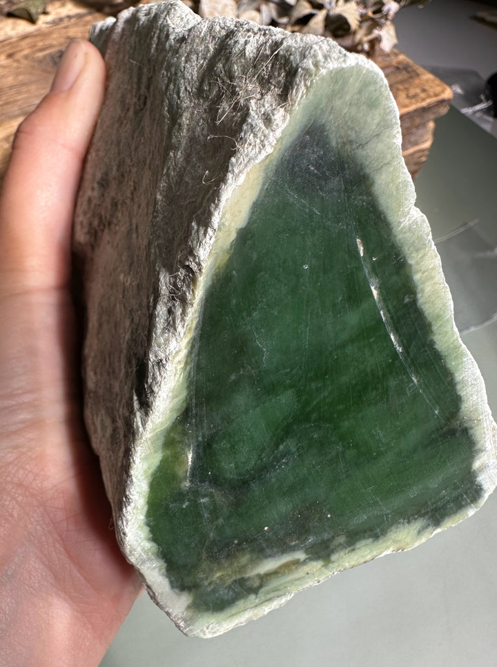 Hand-held Siberian nephrite rough with green interior and rough gray crust.