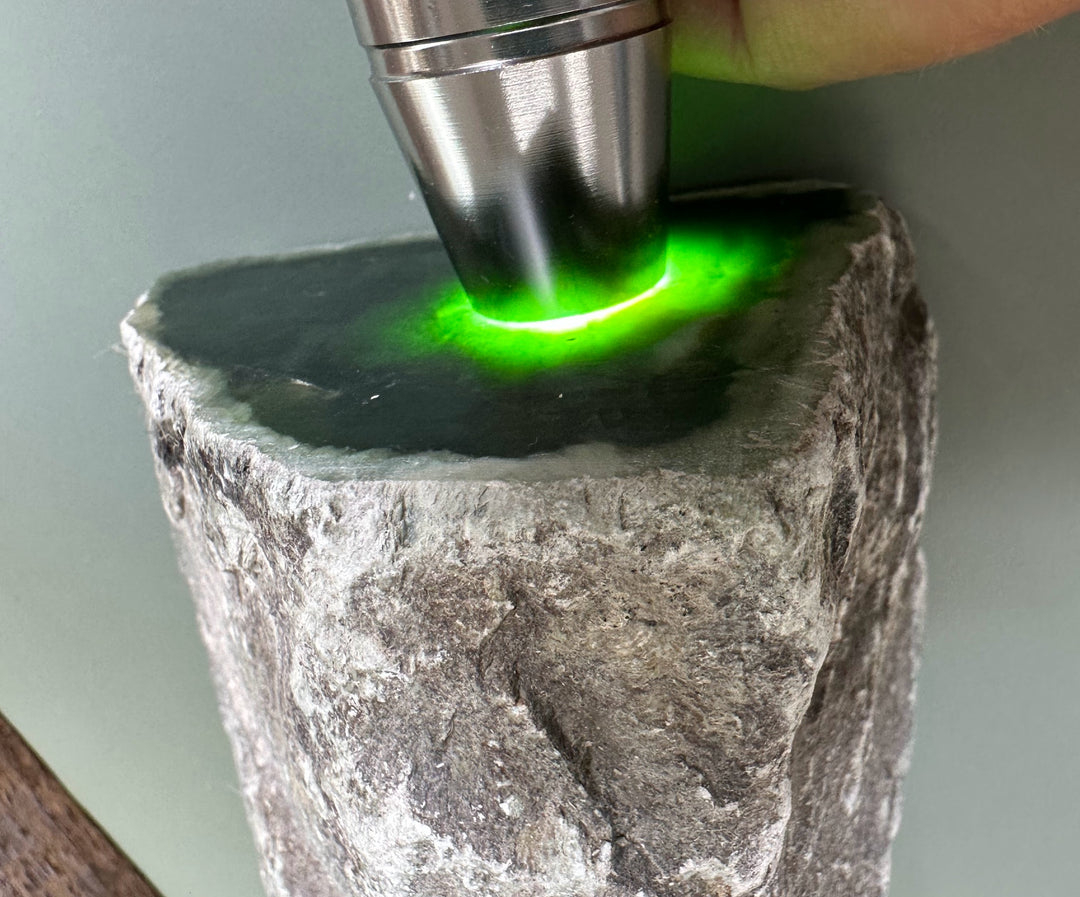 Metal tool touching a green nephrite slab with a bright green glow on the surface.