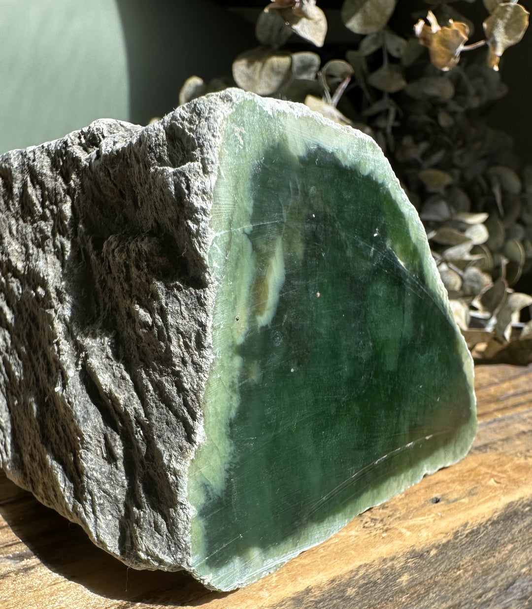 Close up of Siberian nephrite rough showing green interior against a rugged gray rind.