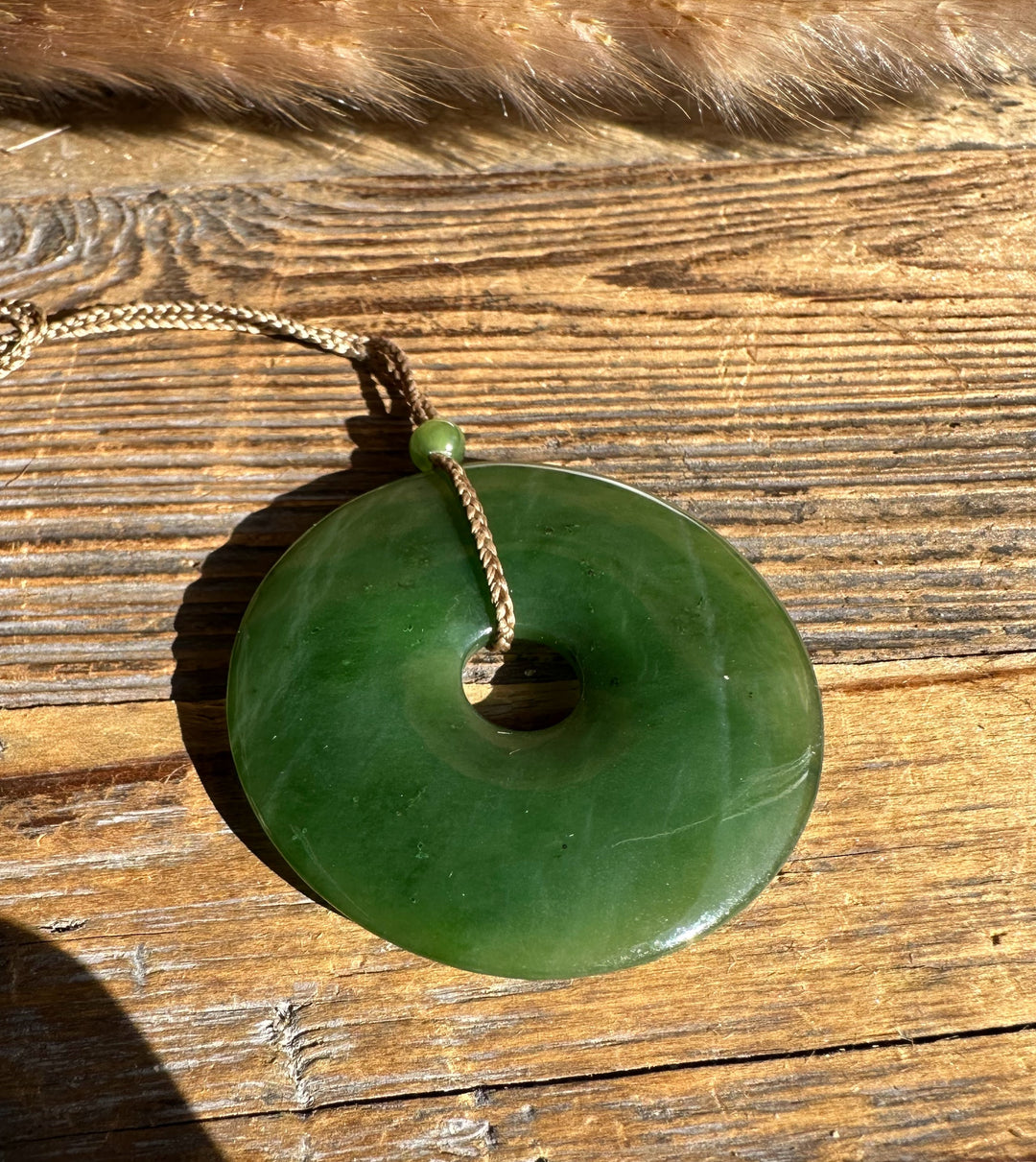 Green jade donut pendant 45mm on a braided brown cord with a small bead, placed on weathered wood.