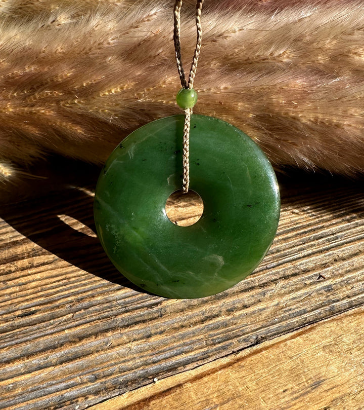 Canadian Jade PI Donut 45mm pendant resting on wood with the braided cord looped through the center hole.