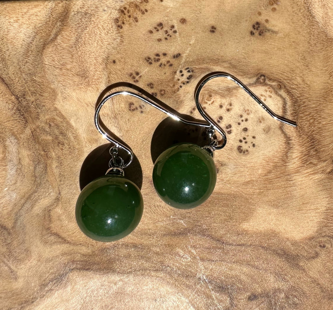 Two Canadian Jade Earrings with 10mm green jade beads and silver hooks resting on a wooden surface