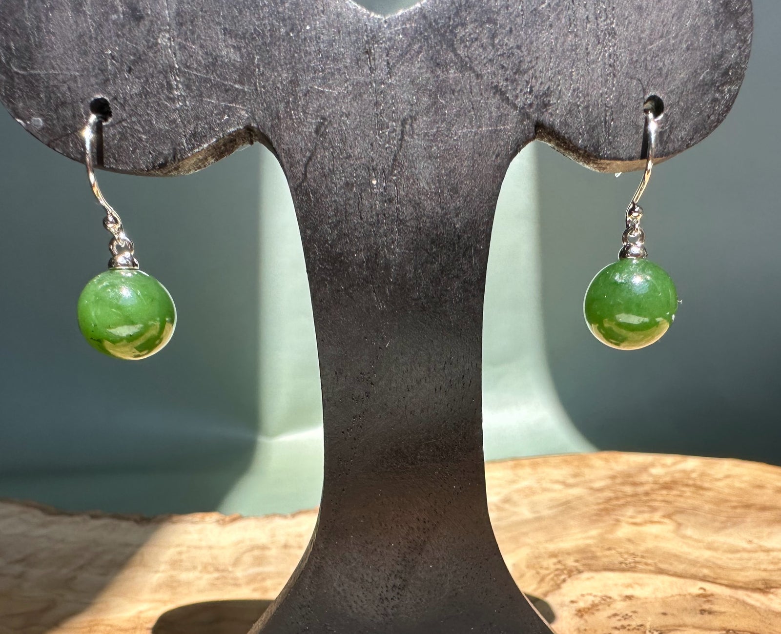 Canadian jade earrings with 10mm green beads hanging from silver hooks on a dark display stand