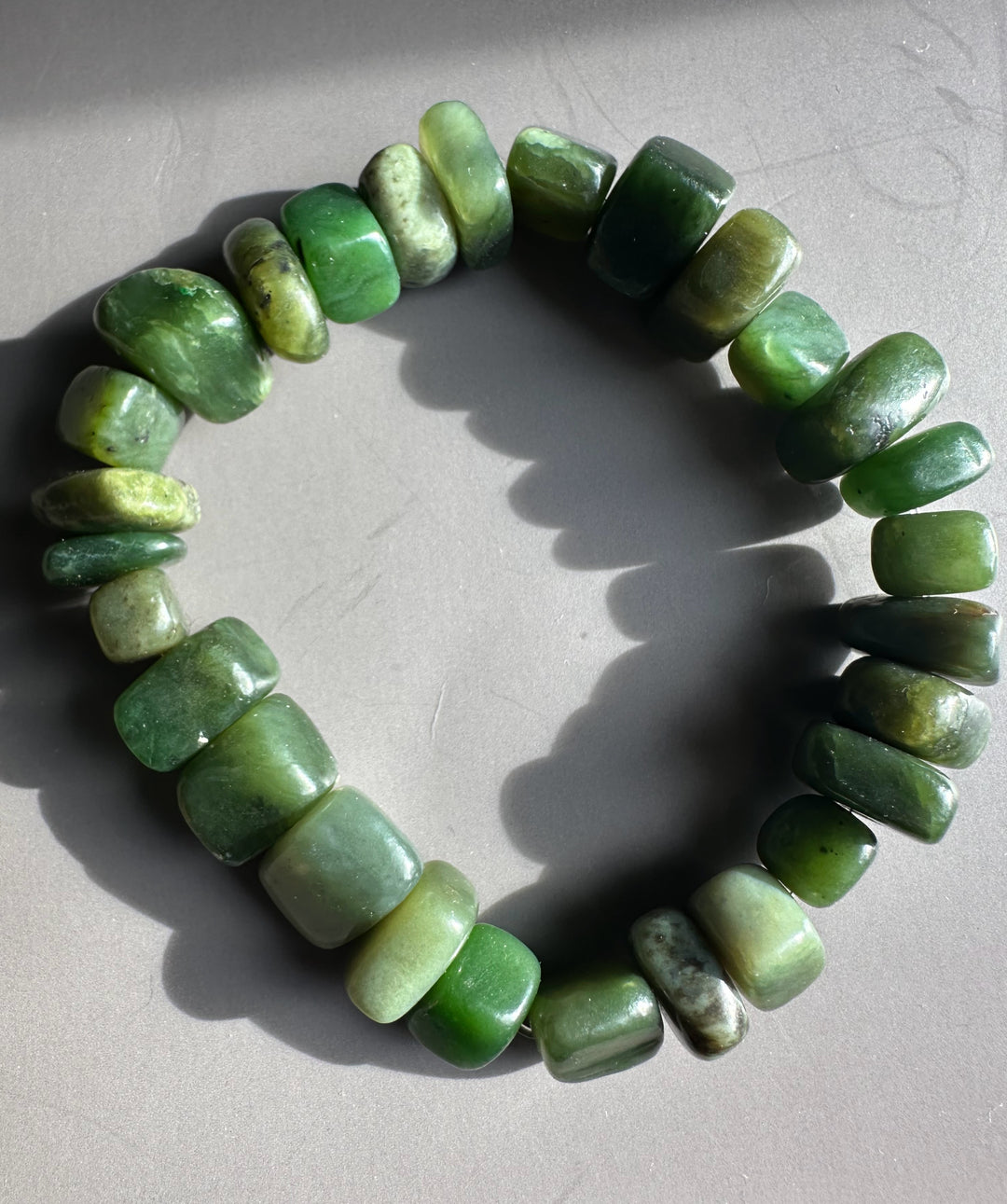 Satin finish green nugget bracelet laid in a circle on a light gray surface