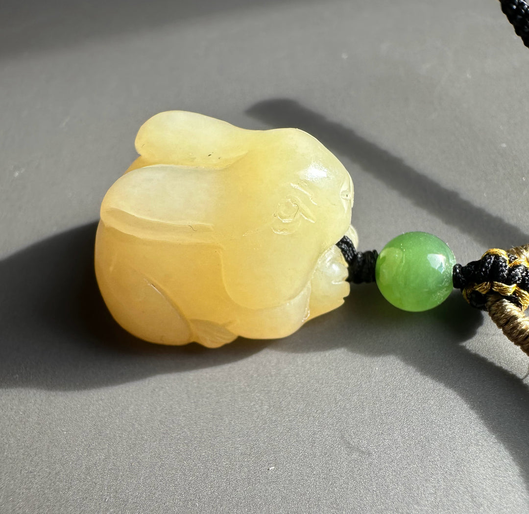 Honey nephrite bunny pendant paired with a green jade bead on a black and gold knotted cord