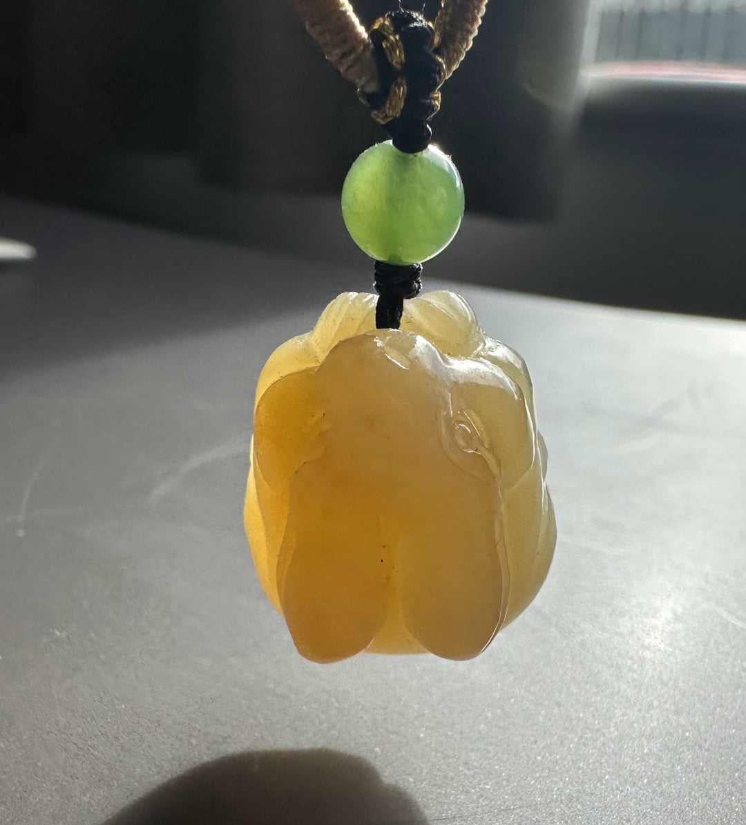 Close up of honey nephrite bunny pendant with green jade bead on a braided cord