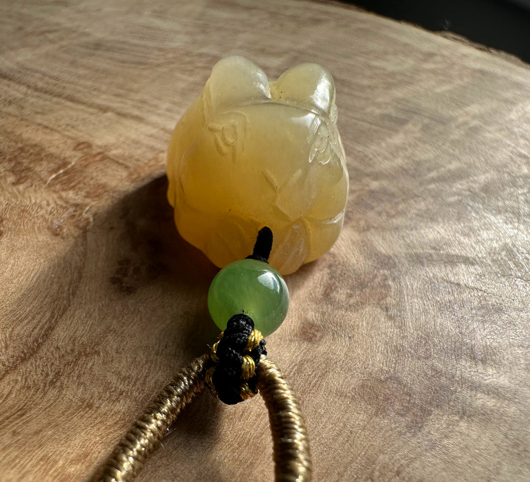 Honey nephrite jade bunny pendant with a green round bead on a knotted cord against a wood surface.