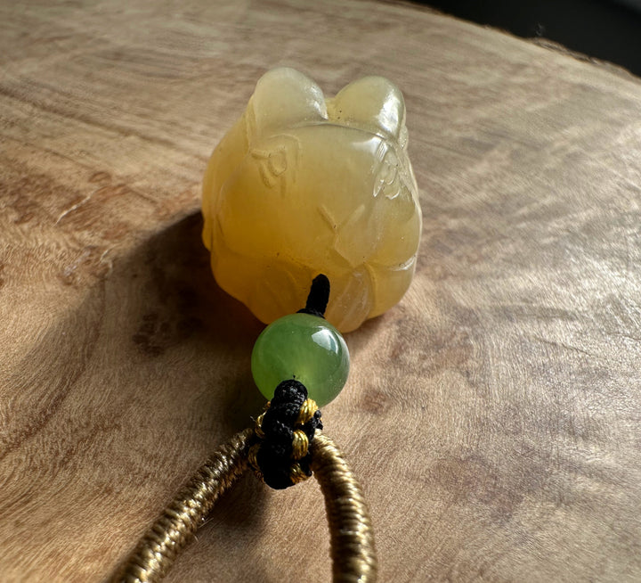 Honey nephrite jade bunny pendant with a green round bead on a knotted cord against a wood surface.