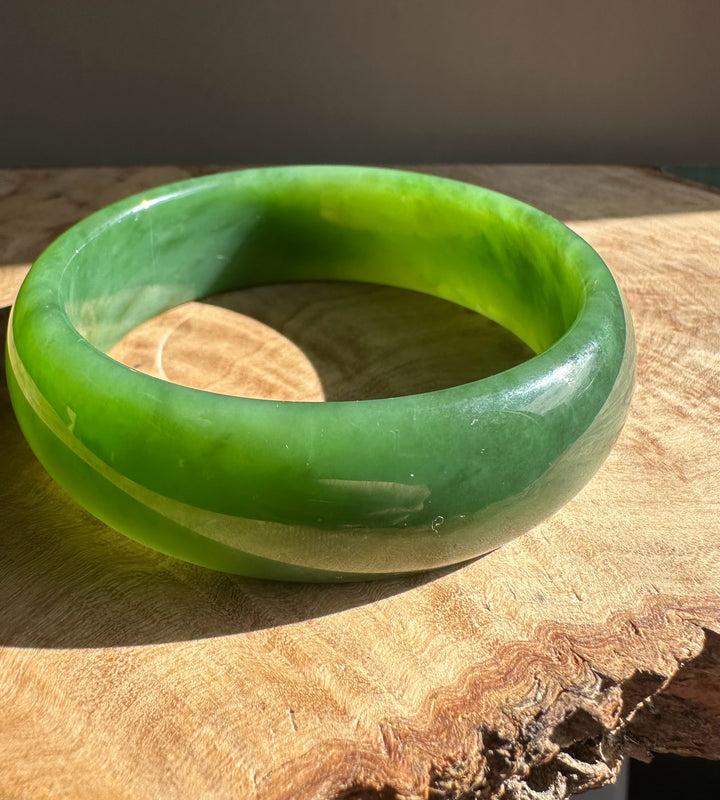 AA Grade Siberian Bangle 60 x 19mm in translucent green jade angled on a wooden surface