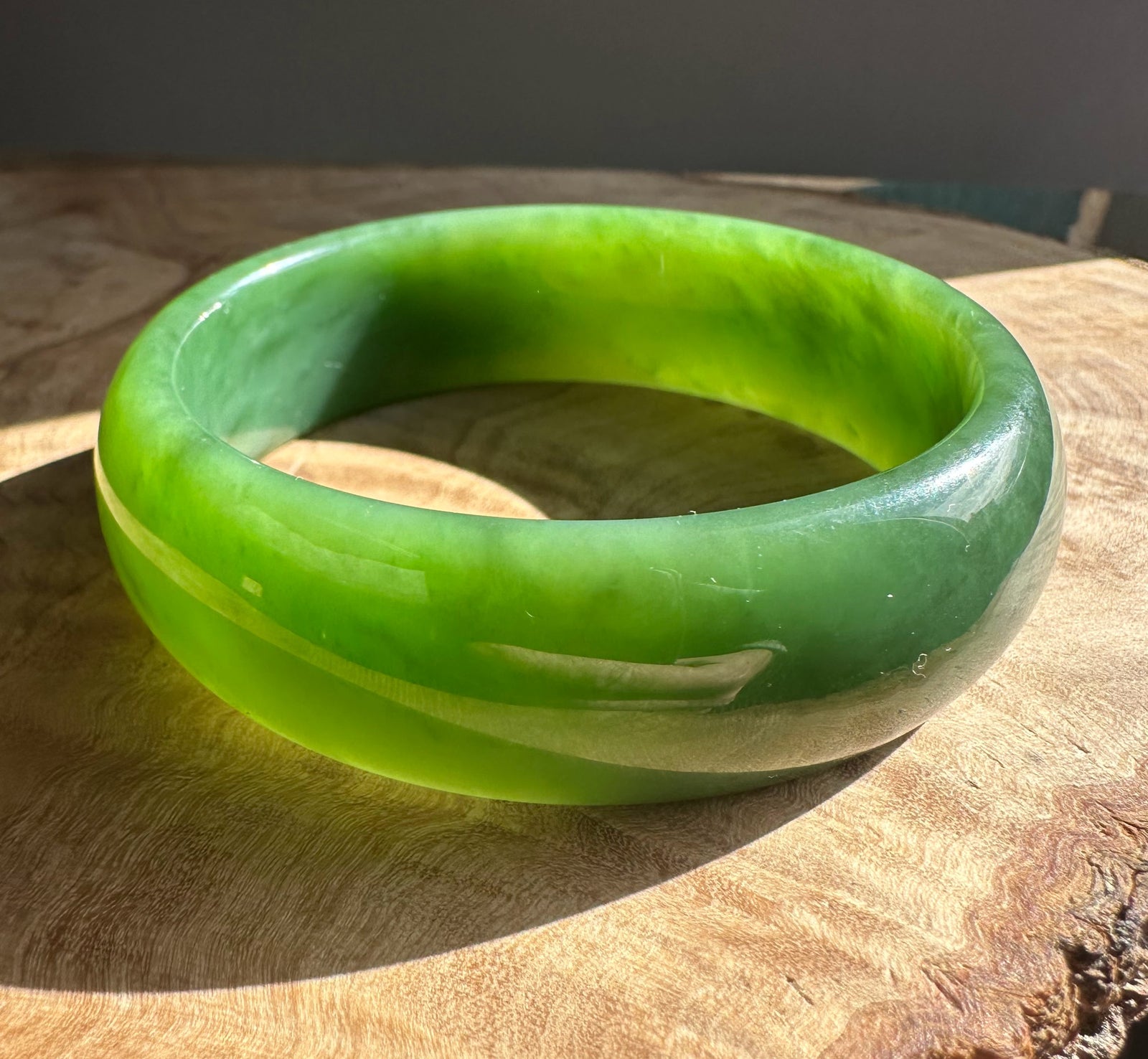 AA Grade Siberian Jade Bangle with vivid green tones displayed on a wooden surface