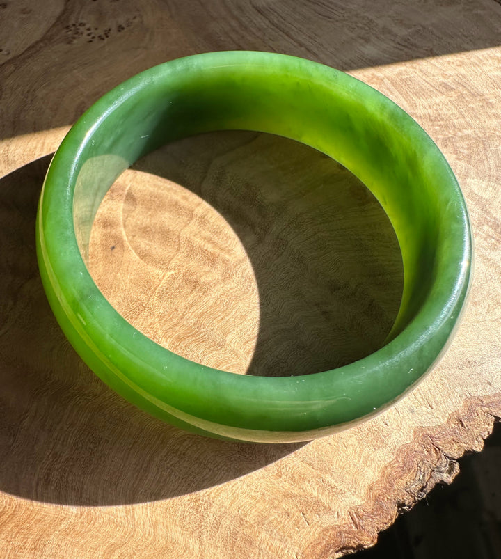 AA Grade Siberian Bangle 60 x 19mm in bright green jade on a wooden surface viewed from above