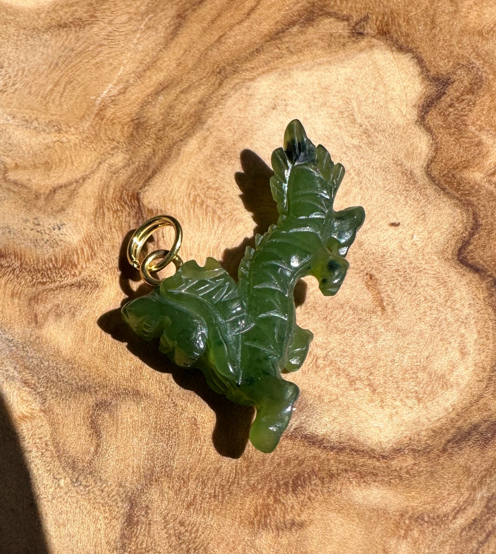 Close-up of green jade dragon pendant with gold bail on wood surface