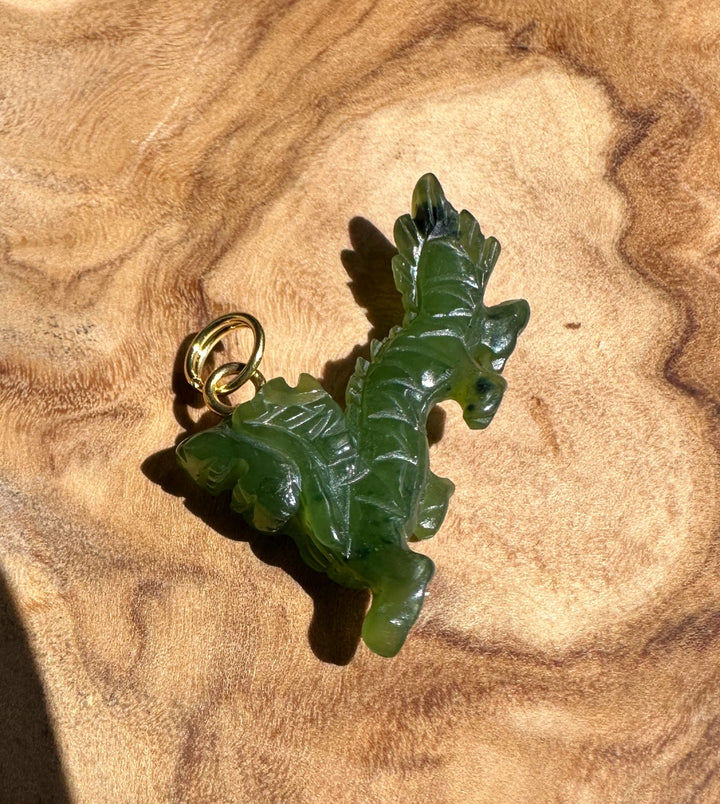 Close-up of green jade dragon pendant with gold bail on wood surface