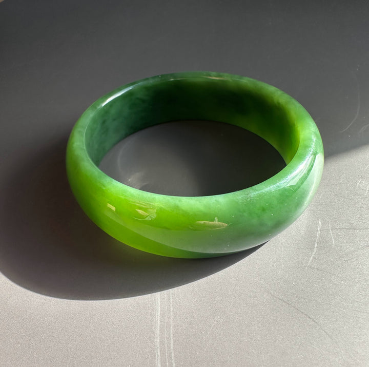 AA Grade Siberian Bangle 60 x 19mm in bright green jade, a polished circular bracelet resting on a gray surface.