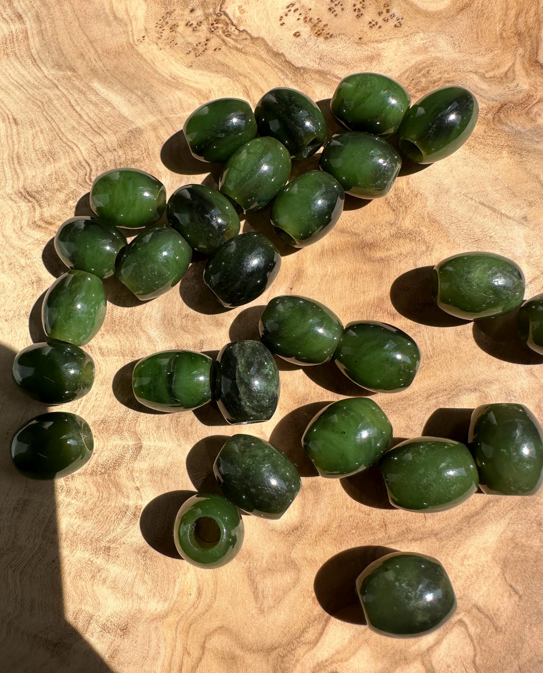 Green jade barrel beads with holes scattered on a wooden surface