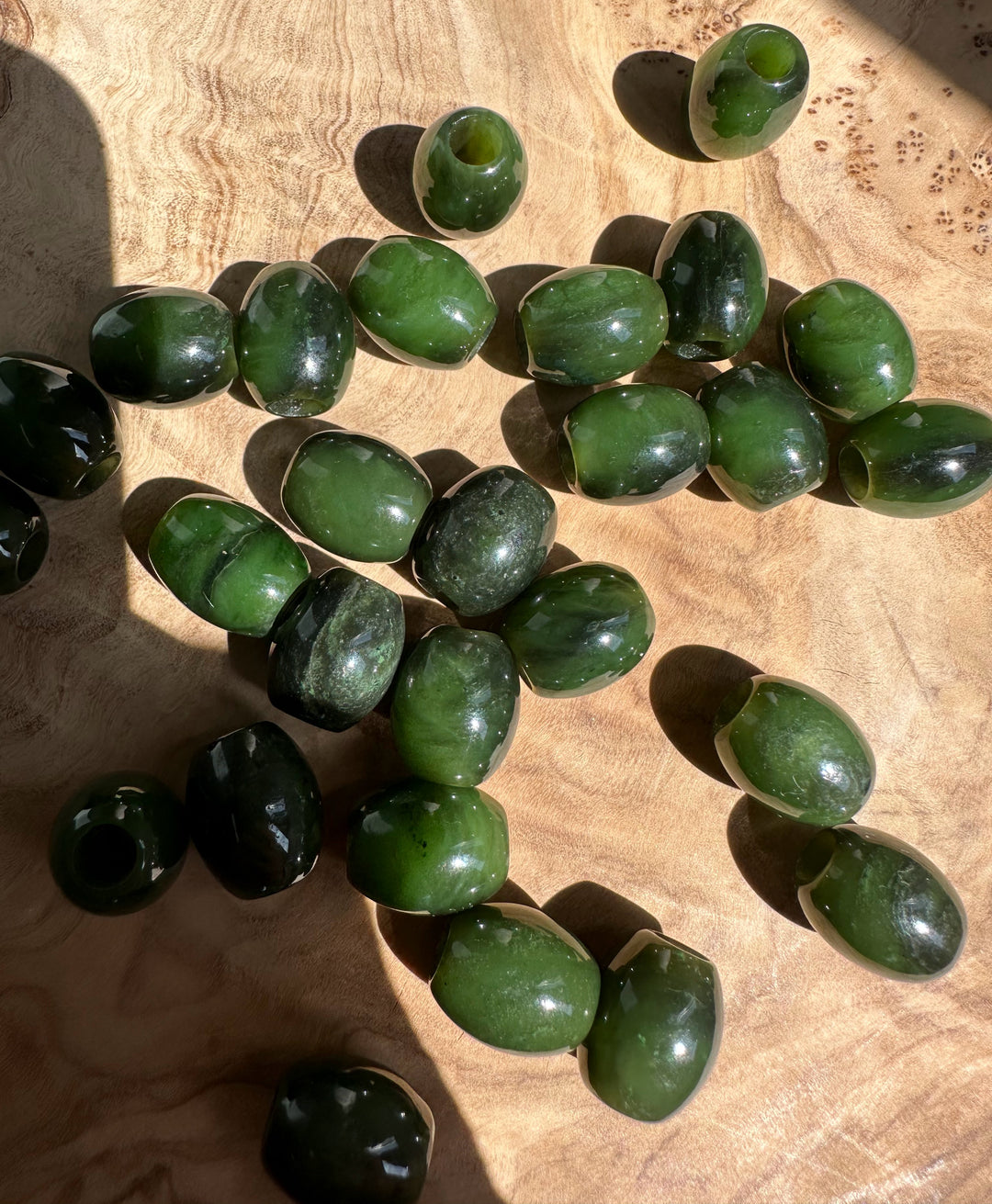 Close up of green jade barrel beads 15x12mm with holes on a wooden surface
